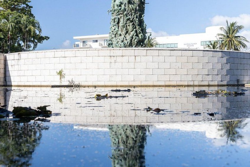 A statue in a reflective pool with a brick wall and a building in the background. 2