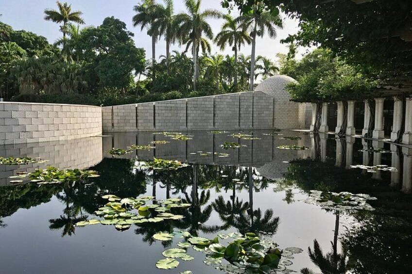 A calm water body with lily pads, a stone wall, and palm trees in the background. 5
