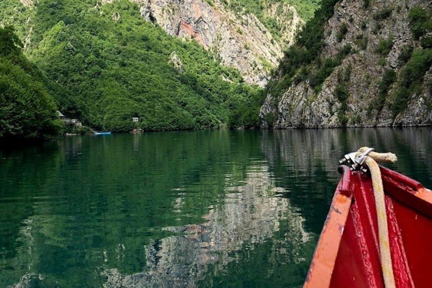 A calm river with a red boat, lush green hills, and rocky cliffs in the background. 5