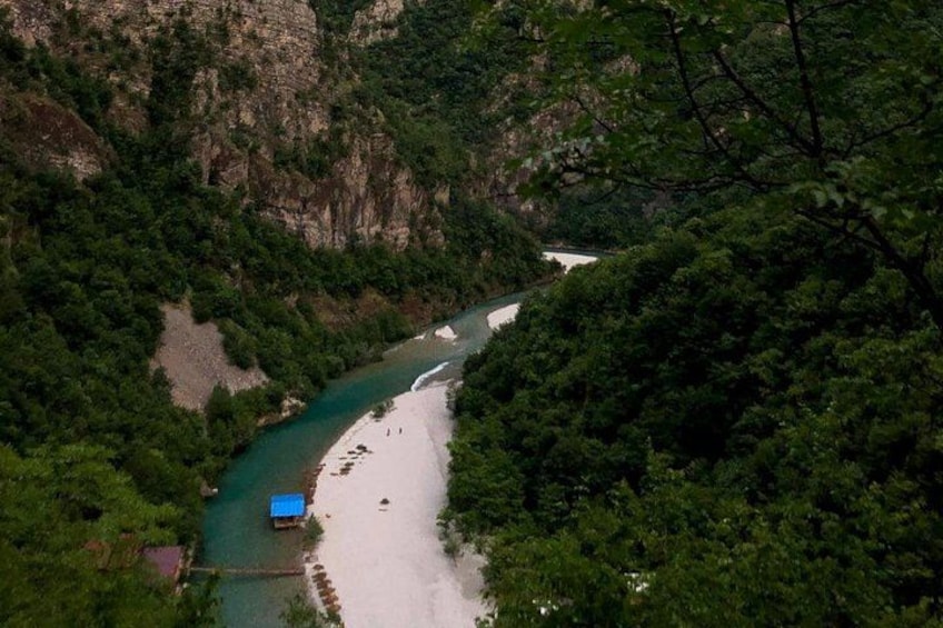 A river winding through a forested valley with a sandy beach and a small blue boat. 2