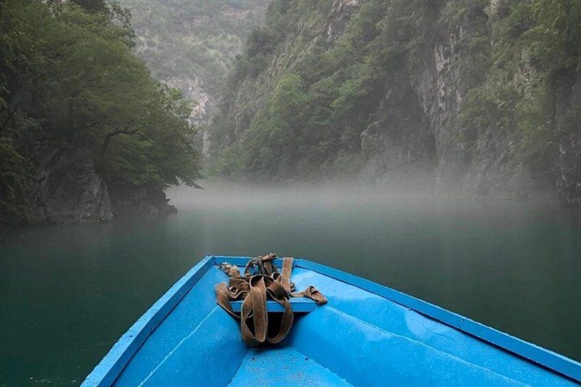 A blue boat with a pile of shoes on the deck, surrounded by misty, green forested cliffs. 4