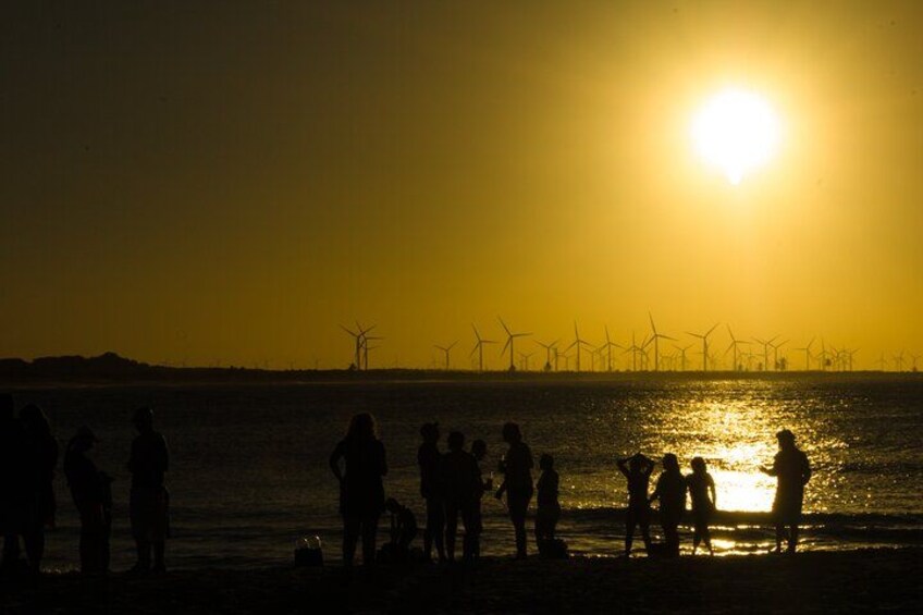 Silhouettes of people on a beach at sunset with wind turbines in the background. 2