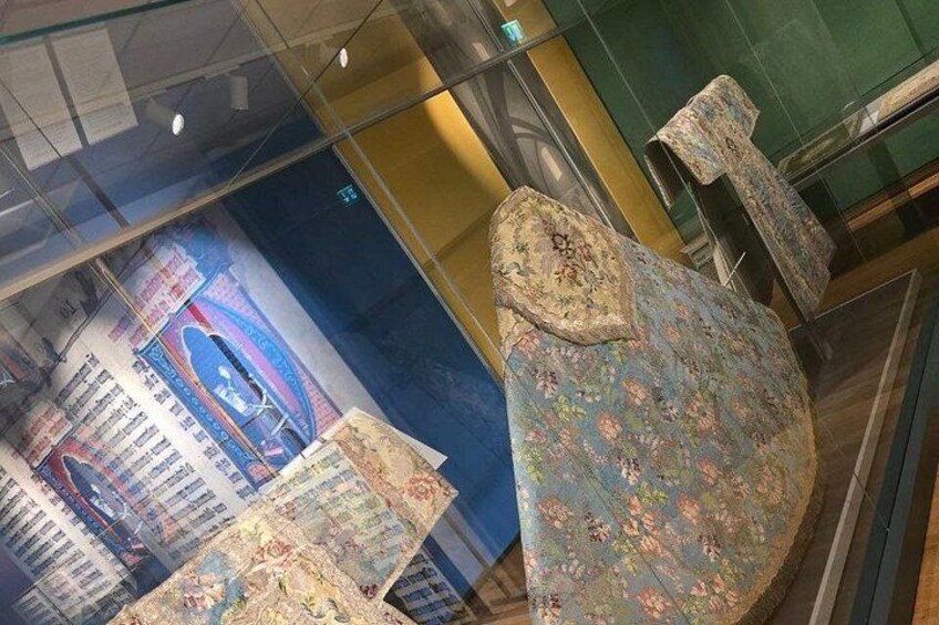 A museum exhibit with a large, ornately decorated chair and a poster in the background. 4