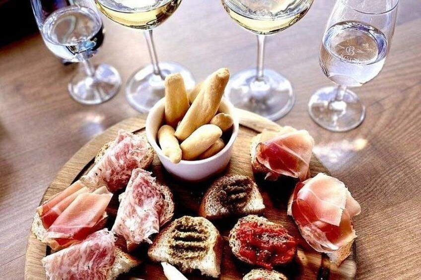 A charcuterie board with various meats and bread, accompanied by glasses of white wine. 3