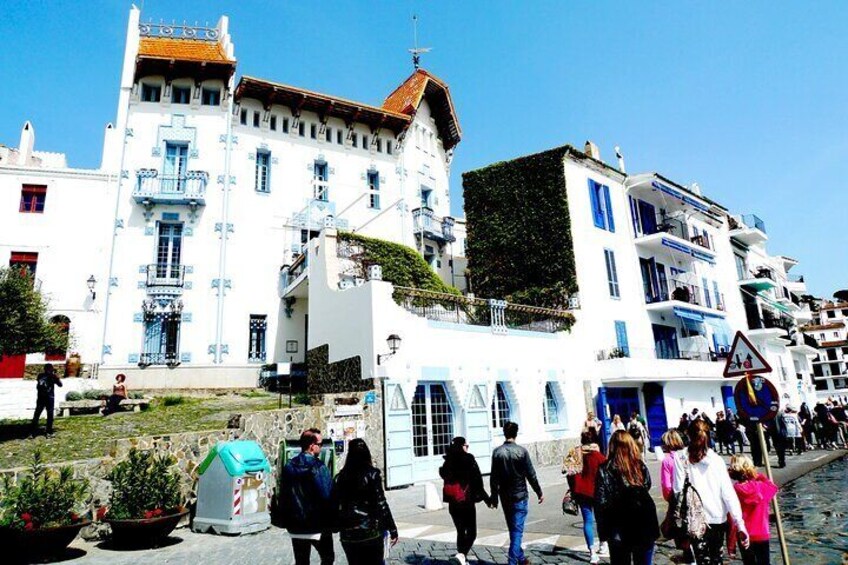 A street with people walking, white buildings with blue accents, and a clear sky. 2