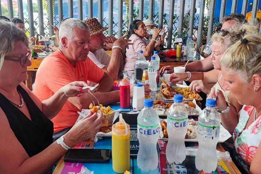 People dining at an outdoor restaurant with tables, chairs, and various food items. 4