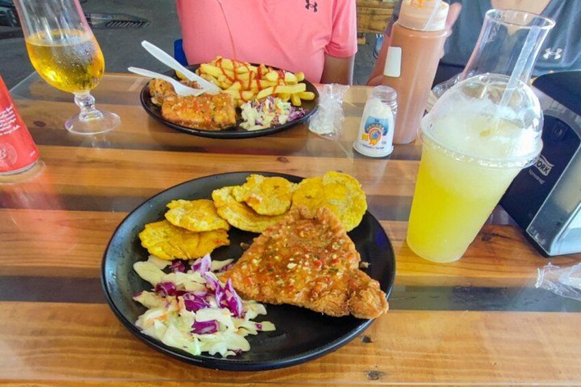 A wooden table with two plates of fried food, a glass of beer, and a drink with a straw. 3