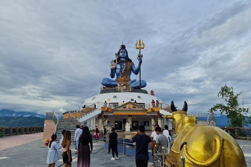 A large statue of a deity with a trident, a golden bull statue, and a temple with steps leading up to it. 1