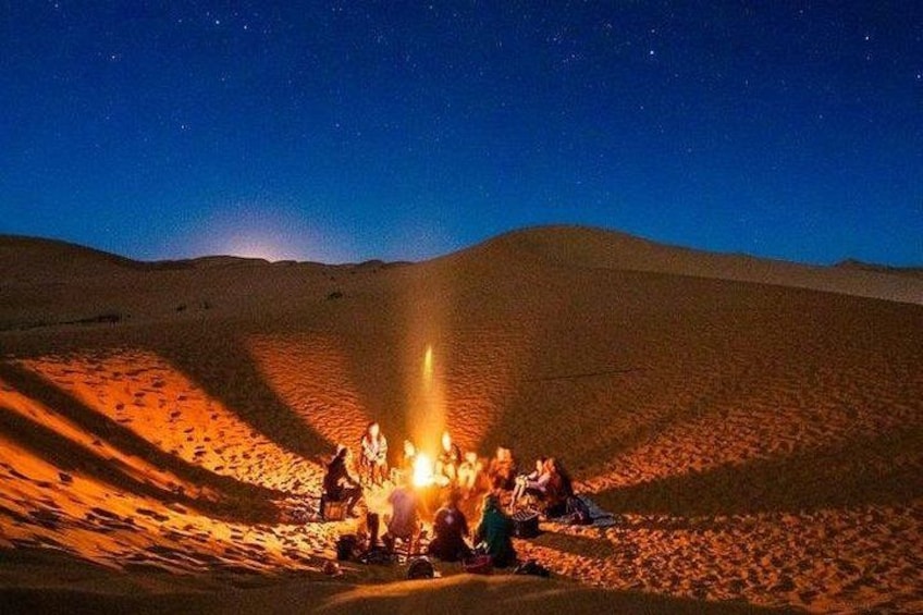 A group of people gathered around a fire in a desert at night. 4