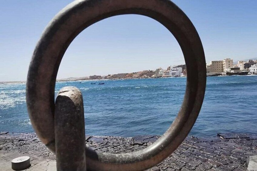 A metal ring structure in the foreground with a coastal cityscape in the background. 3