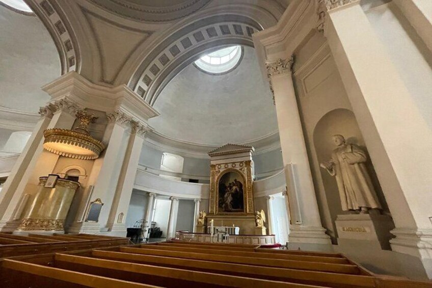 An interior of a church with high ceilings, ornate columns, and a central altar. 2