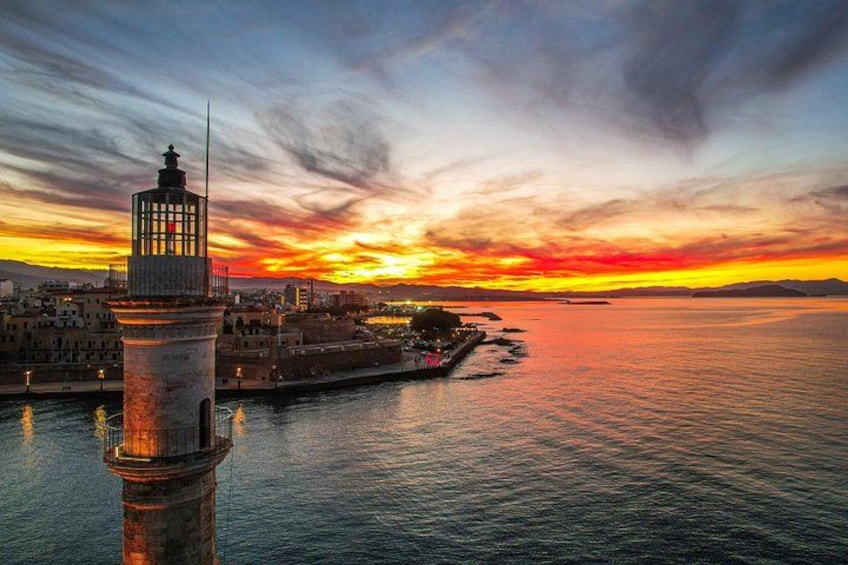 Un paysage urbain côtier au coucher du soleil, avec un phare imposant, des eaux calmes et une côte lointaine. 1