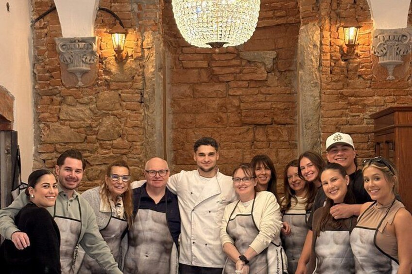 Eine Gruppe von Personen in Schürzen steht vor einer Steinwand mit einem Chandelier. 2