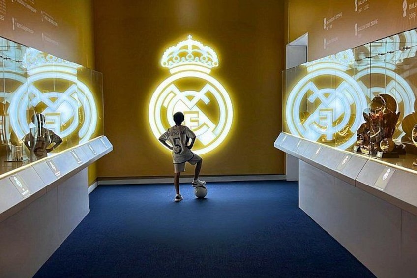 A person in a sports uniform practicing soccer kicks in front of illuminated Real Madrid logos. 3