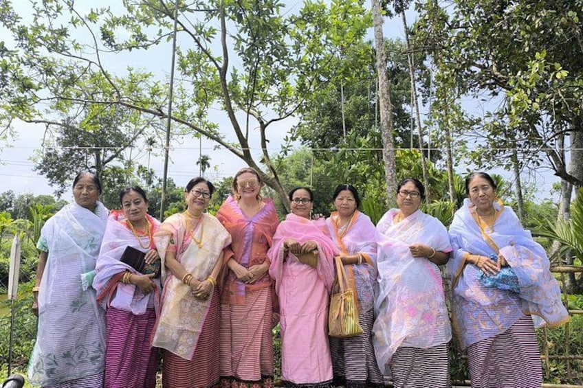 A group of people standing outdoors, dressed in traditional attire, with trees and a clear sky in the background. 1
