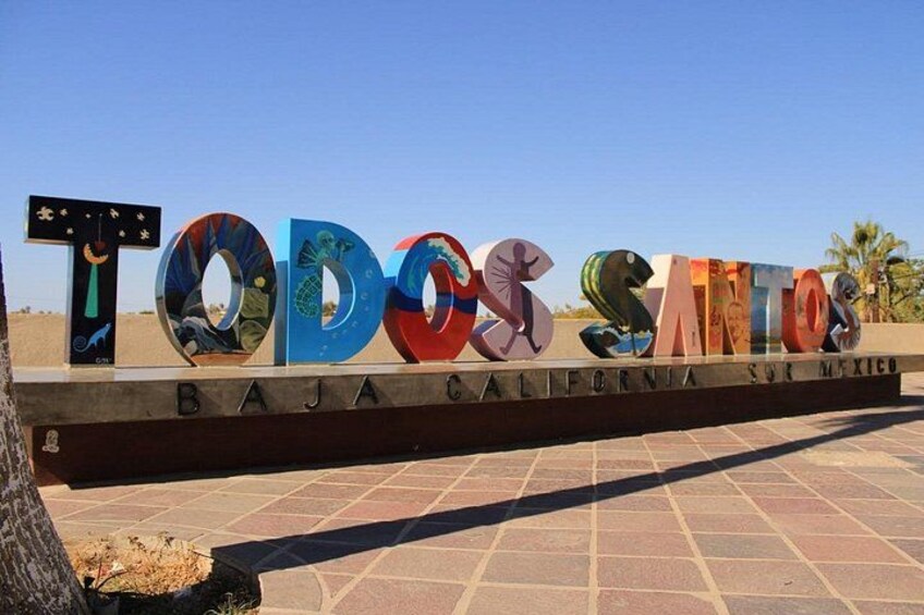 Un letrero con letras de colores que deletrean 'TODOS SANTOS' y 'BAJA CALIFORNIA SUR MEXICO' debajo. 3