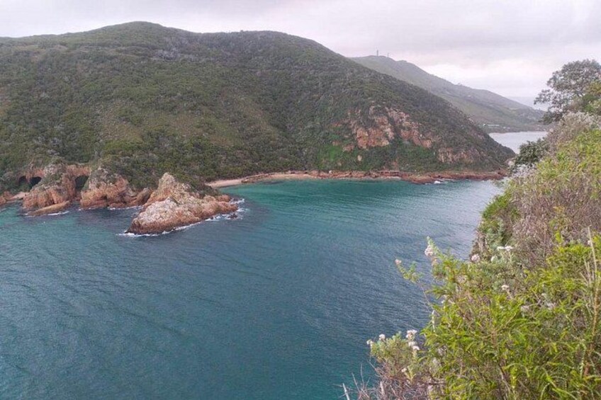A coastal landscape with a clear blue sea, rocky outcrops, and green hills. 3