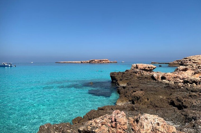 Een kustlandschap met helder turquoise water, rotsformaties en verre bootjes. 3