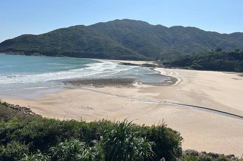 A beach with a clear sky, sandy shore, and green hills in the background. 2