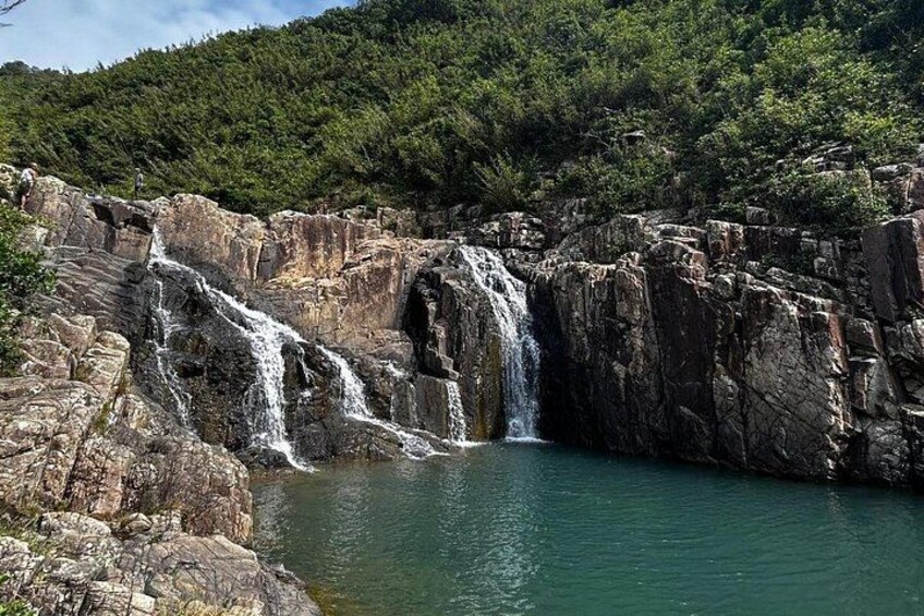A waterfall cascading over rocky terrain into a calm body of water, surrounded by dense forest. 4