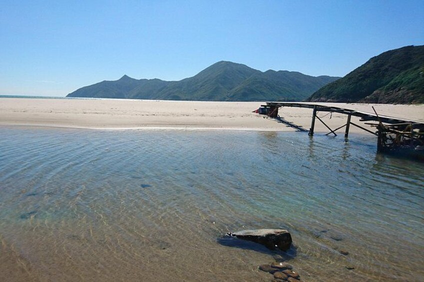 A beach with clear water, a wooden pier, and mountains in the background. 1