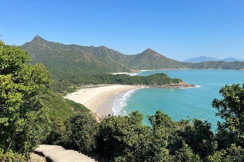 A coastal landscape with a beach, turquoise waters, and green hills. 5