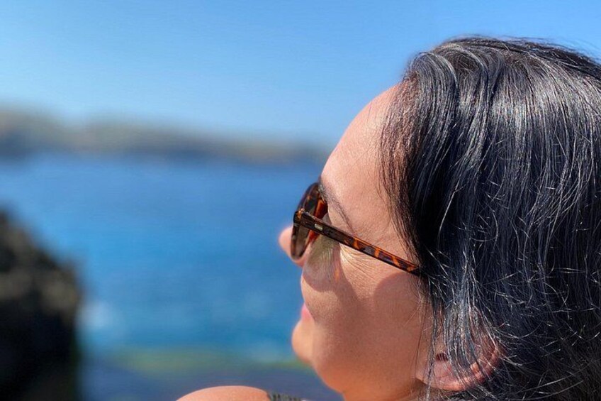 Una persona con capelli scuri e occhiali da sole, che guarda un corpo d'acqua con un litorale roccioso. 5