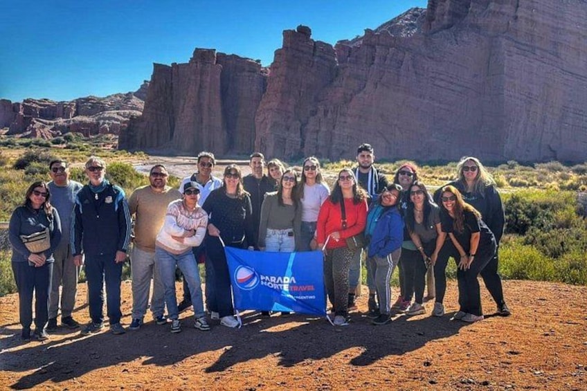 A group of people standing in a desert landscape with red rock formations in the background. 2
