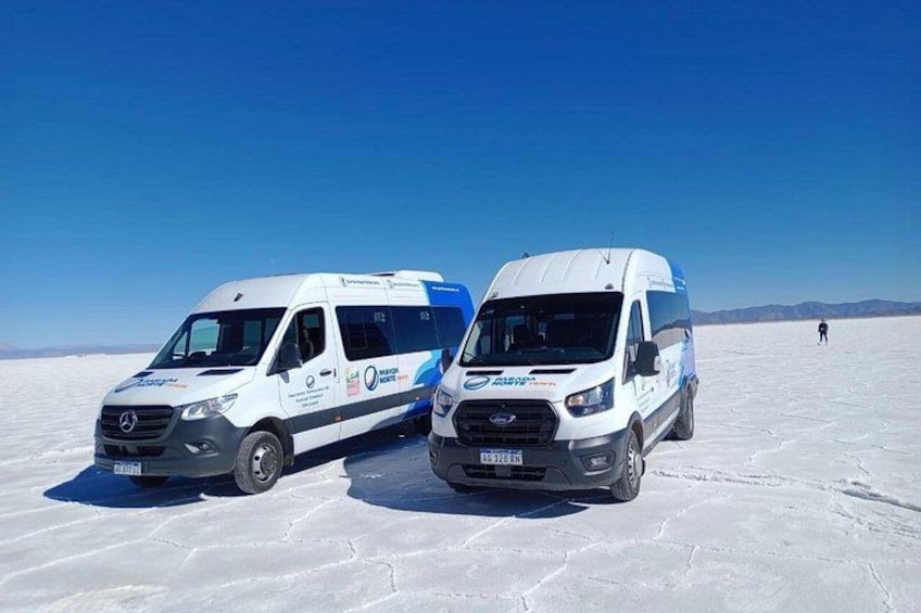 Two white vans parked on a salt flat with a clear blue sky. 3