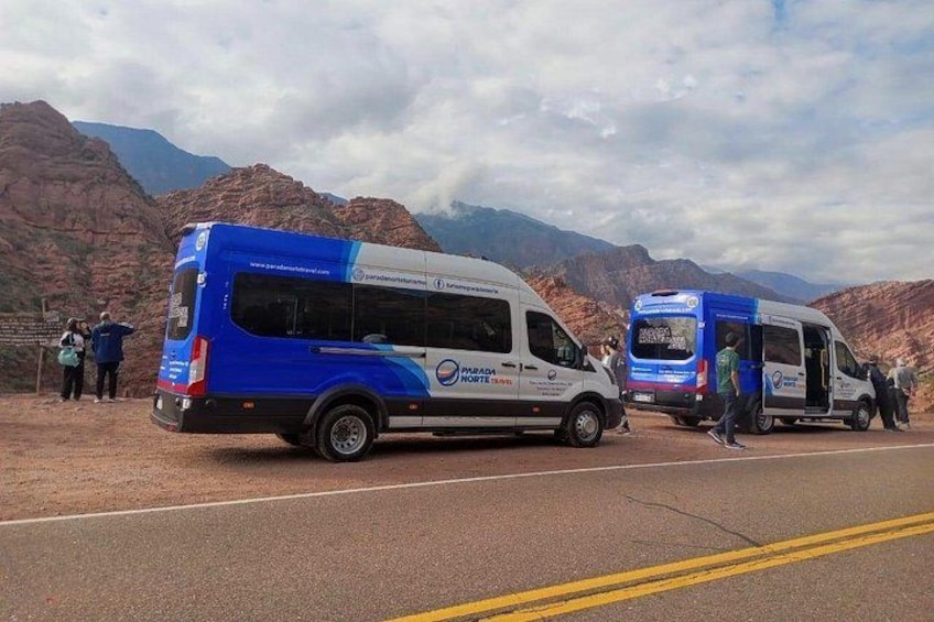 A blue and white bus with 'Paradas del Norte' written on it, parked on a road with mountains in the background. 4