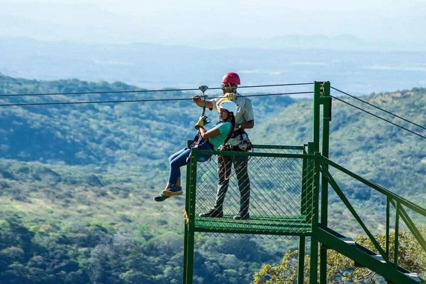 A zip-lining activity with a person in a harness and another person assisting, overlooking a mountainous landscape. 2