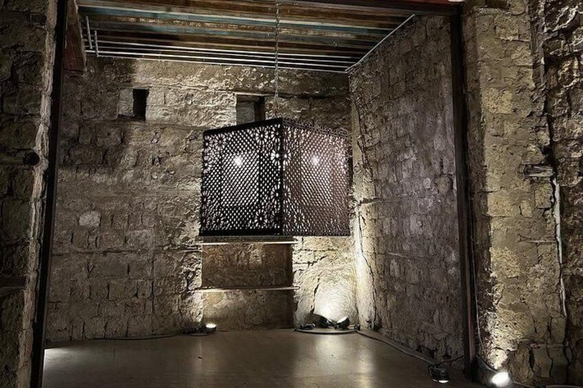 A dimly lit room with stone walls, a metal mesh partition, and a concrete floor. 2