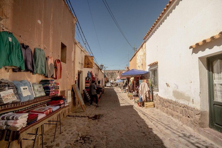 A narrow street with shops on either side, displaying various items for sale. 4