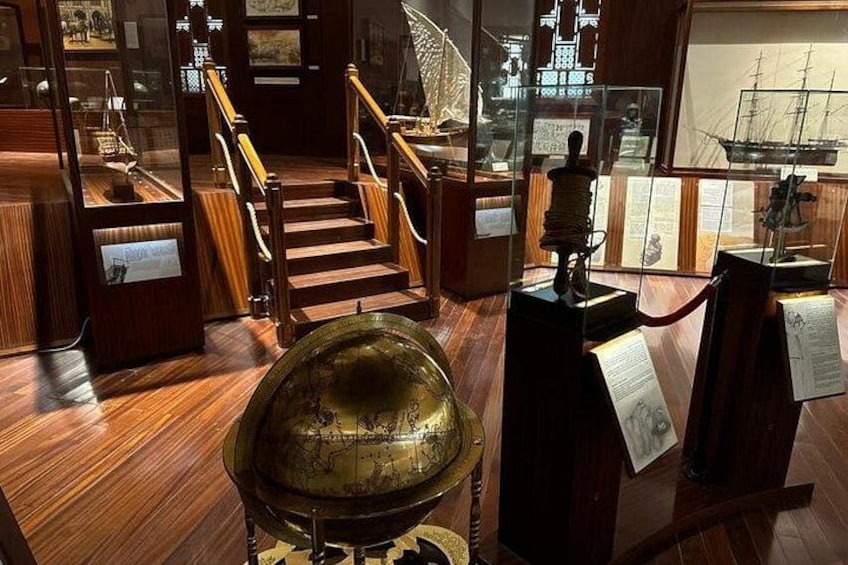 Interior de museo con suelos de madera, un globo de latón, una maqueta de barco y una escalera. 2