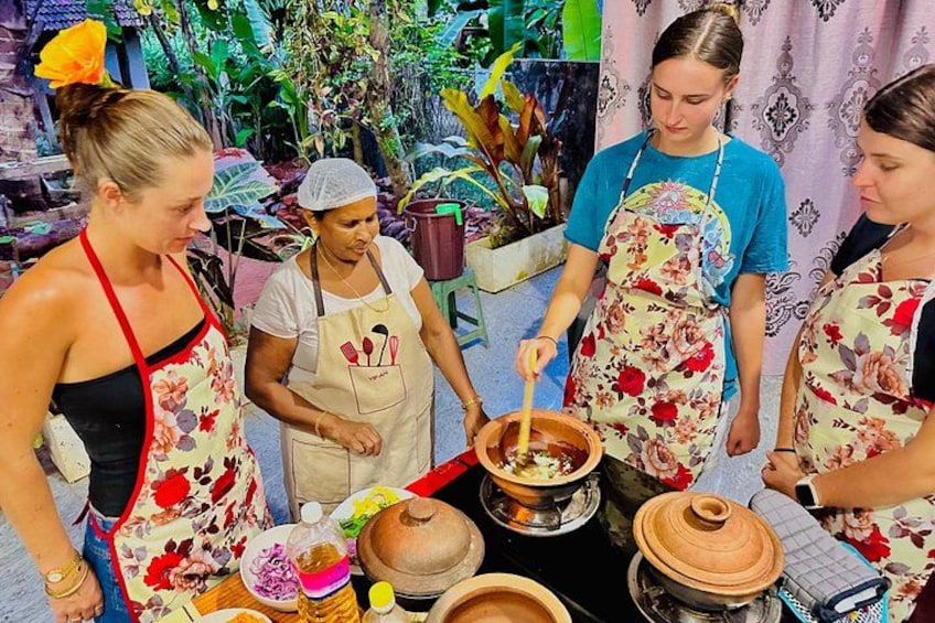 Quatre personnes, portant des tabliers, cuisinent en plein air avec des casseroles et des légumes. 1