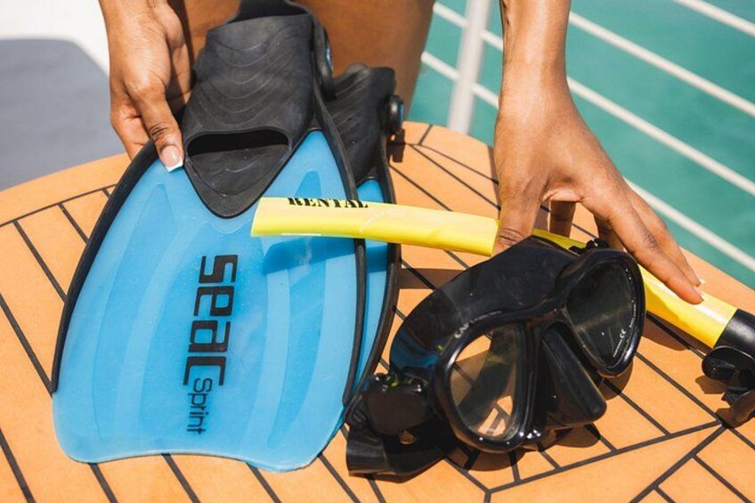 Una tabla de surf azul, aletas negras y un snorkel amarillo sobre una superficie de madera. 3