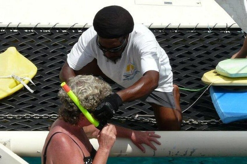 A person in a pool with a snorkel and mask, another person assisting them, and a boat in the background. 2