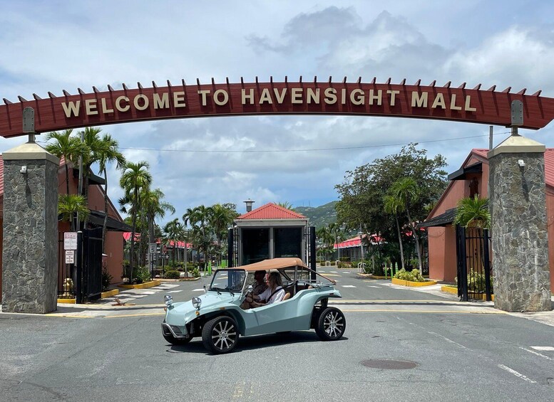 A light blue convertible car driving through a mall entrance with a 'Welcome to Havensight Mall' sign. 2