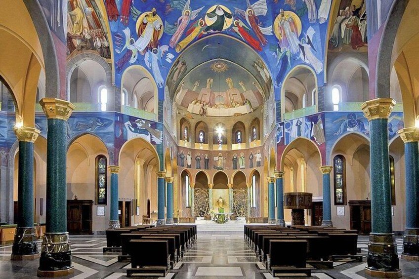 Interno di una chiesa con soffitti a volta, affreschi colorati e file di bancali. 3