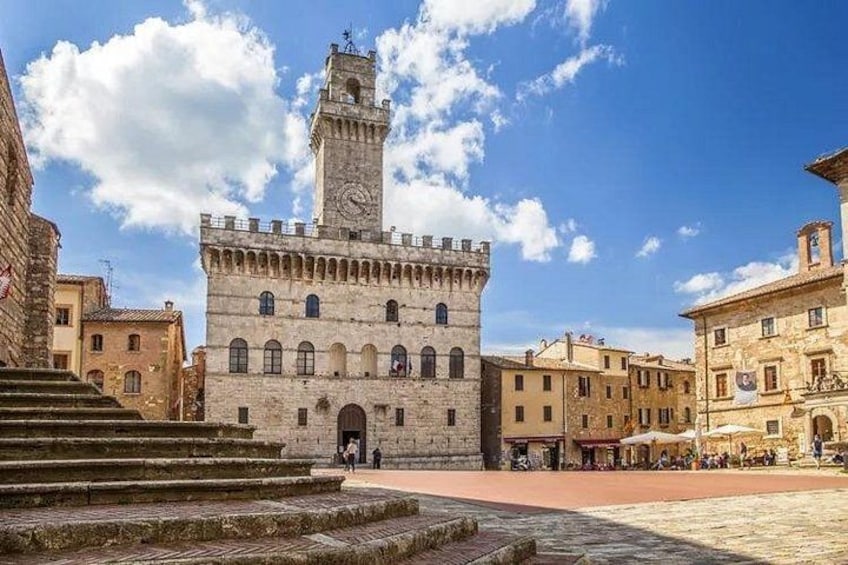 A historic stone building with a clock tower, steps leading up to it, and surrounding buildings. 1