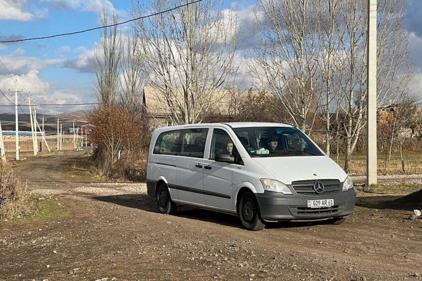 A white van parked on a dirt road with leafless trees and power lines in the background. 3