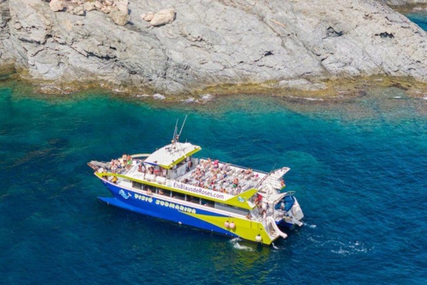 A boat with people on it, floating on clear blue water near rocky shores. 1
