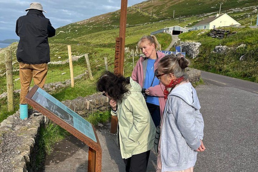 A group of people standing by a signpost on a rural road with a stone wall and grassy landscape in the background. 3
