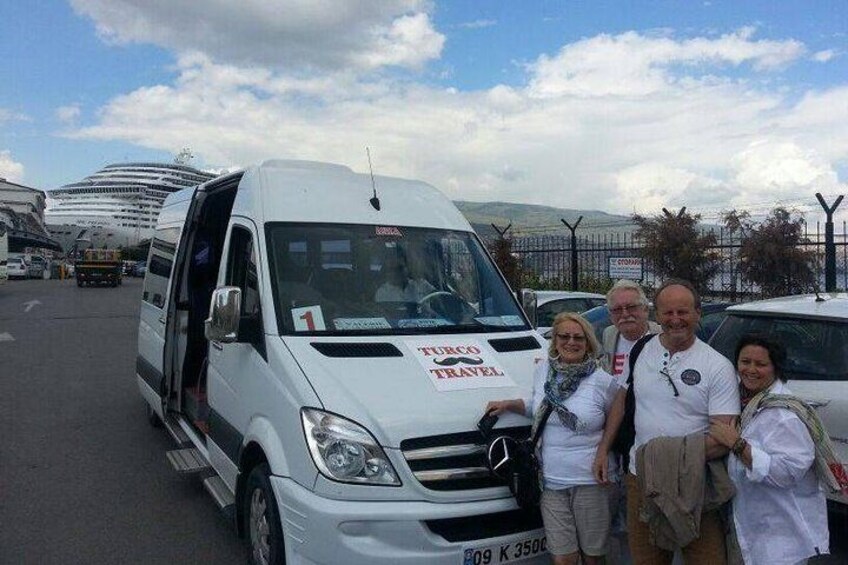 Ein weißer Van mit dem Schriftzug 'TURBO TRAVEL' auf der Seite steht an einer Straße, im Hintergrund ist ein Kreuzfahrtschiff zu sehen. 1