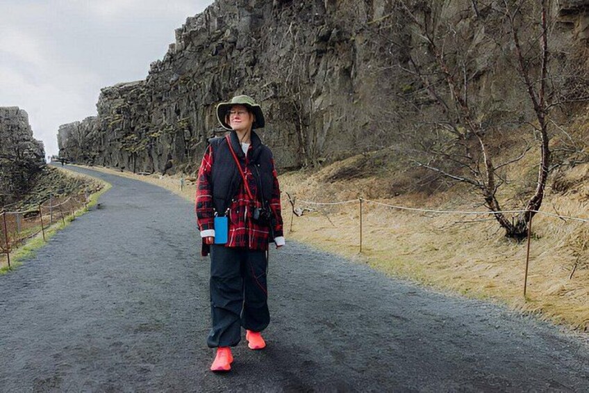 A person walking on a paved path with rocky cliffs and sparse vegetation. 2