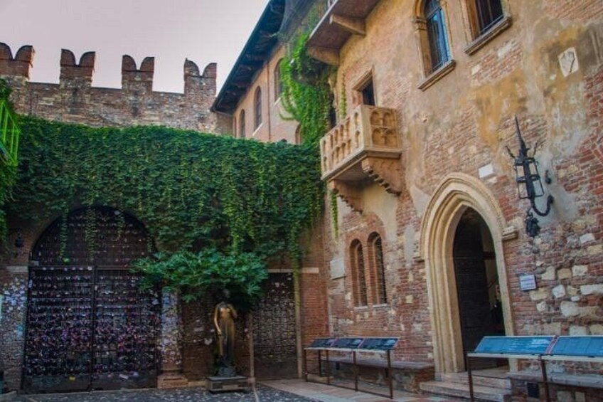 A historic building with ivy-covered walls, a large arched entrance, and a balcony. 3