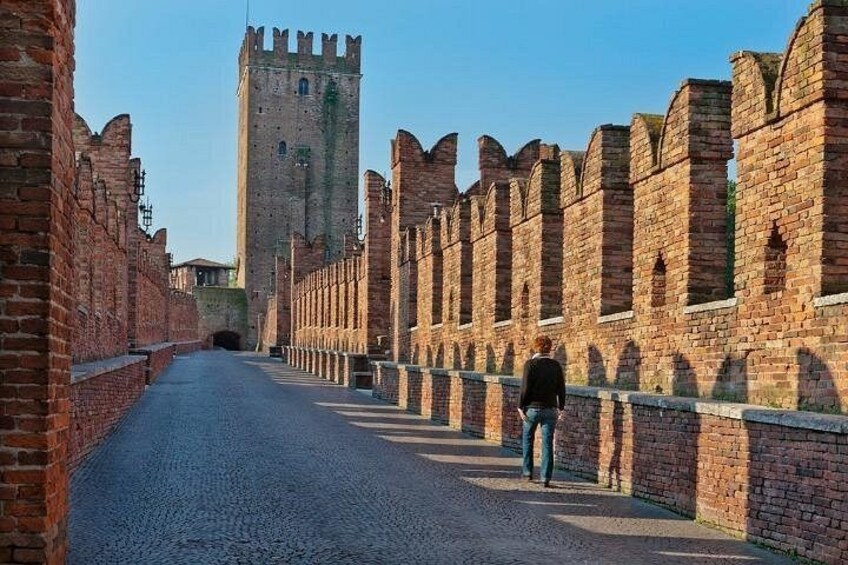 A cobblestone street flanked by brick walls and a tower. 2