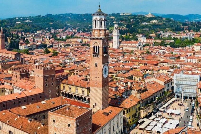 A cityscape with a prominent clock tower, historic buildings, and a hilly backdrop. 1