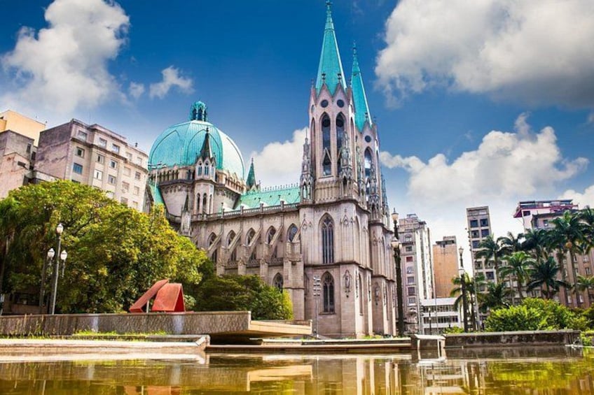 A cathedral with a green dome and a tall spire, surrounded by trees and a body of water. 3