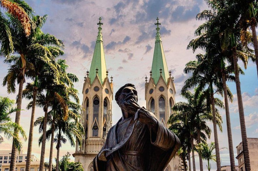 A statue in front of a church with two green spires. 4